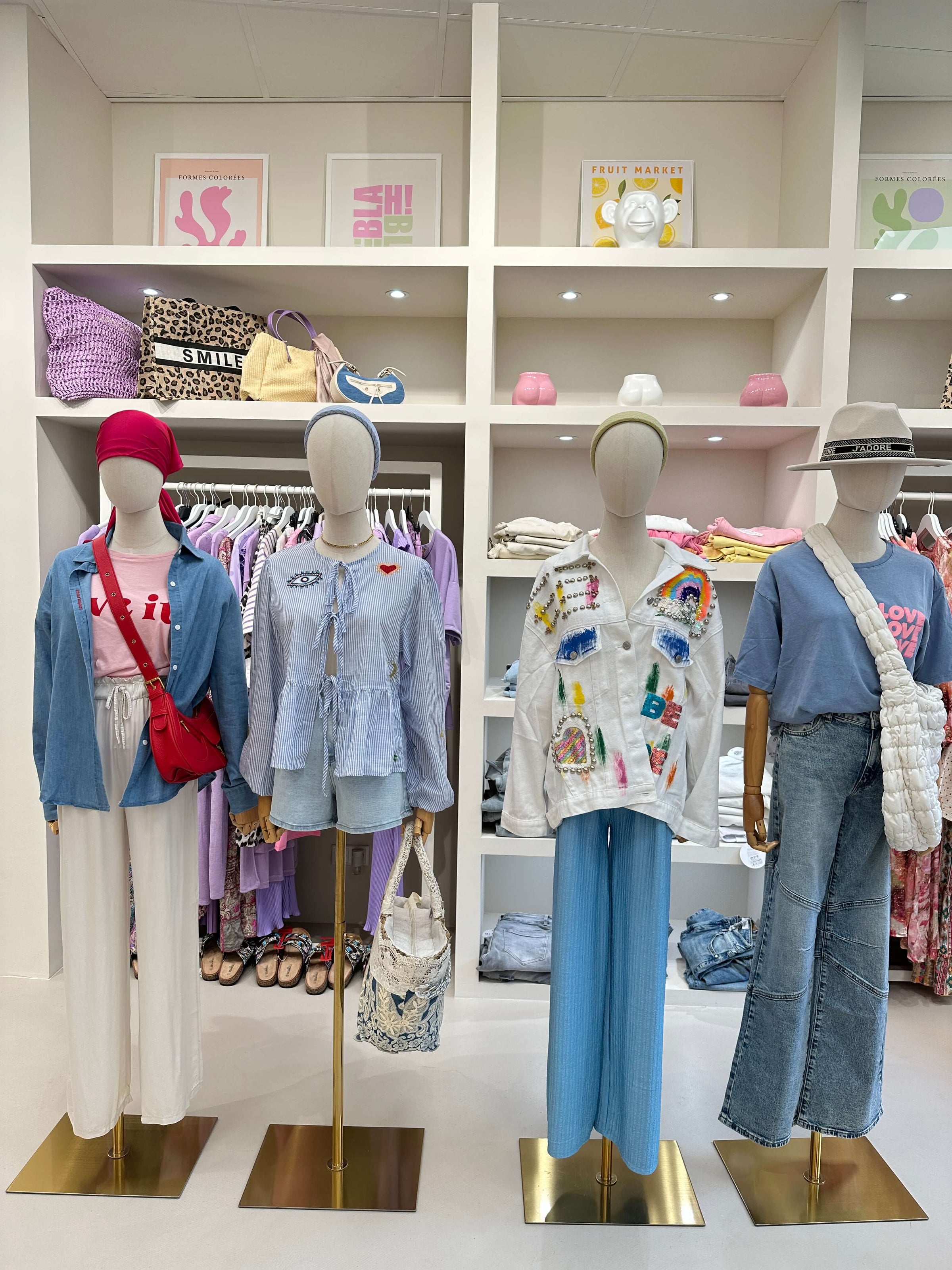 Vier Damen-Outfits aus Lisas Boutique mit Jeans, Print-Shirts, Statement-Blusen und Accessoires wie Taschen und Hüten – modisch präsentiert im Store