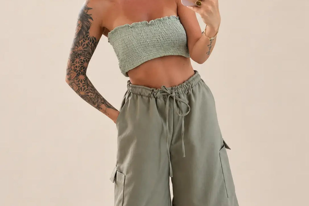 Kobieta w spodniach cargo do kolan w kolorze khaki z wiązanym pasem i naszytymi bocznymi kieszeniami, do tego marszczony top bandeau w kolorze szałwiowym | Lisa’s Boutique
