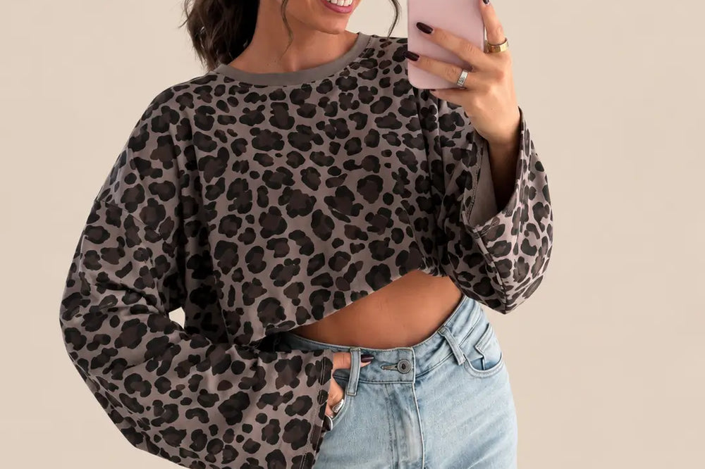 Frau in kurz geschnittenem Longsleeve mit Leoprint in Braun mit weiten Ärmeln, dazu helle Jeans und Sonnenbrille | Lisa’s Boutique