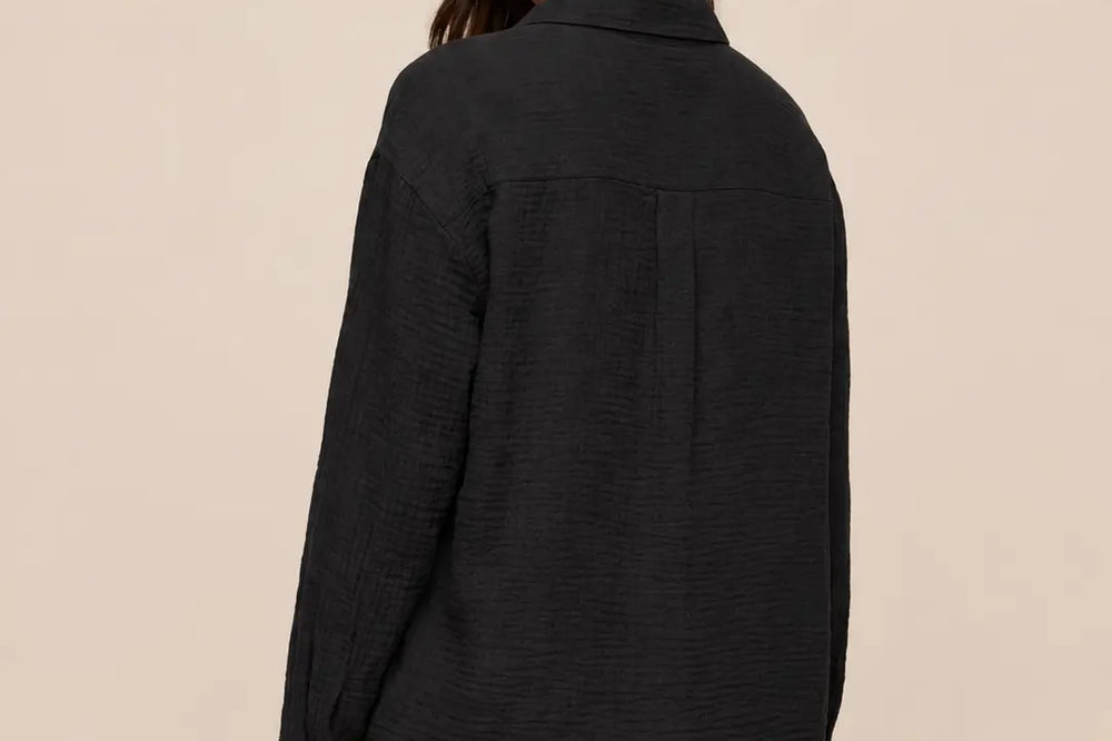 Schwarz kombinieren: schwarze Bluse in Rückansicht mit weißer Hose vor hellem Studiohintergrund | Lisa’s Boutique