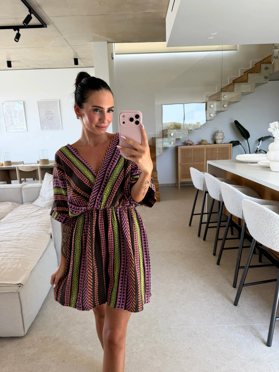 Frau in kurzem Musselin Jumpsuit in Braun/Mix mit V-Ausschnitt, elastischem Bund und grafischem Zickzackmuster in einem hellen Wohnraum | Lisa’s Boutique