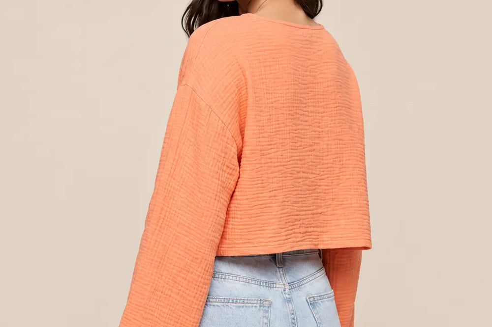Farbkombinationen Kleidung: Oberteil in Apricot zu heller Jeans, Rückansicht vor hellem Studiohintergrund | Lisa’s Boutique