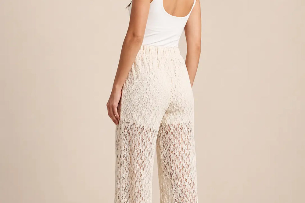 Outfit erstes Date: Frau von hinten in weißem Top und weiter cremefarbener Spitzenhose vor beigem Hintergrund | Lisa’s Boutique