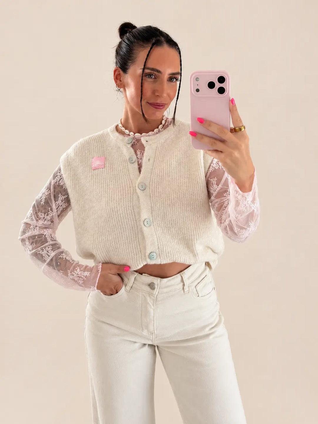 Donna in gilet in maglia beige con bottoni su camicetta rosa in pizzo e pantaloni chiari | Lisa’s Boutique