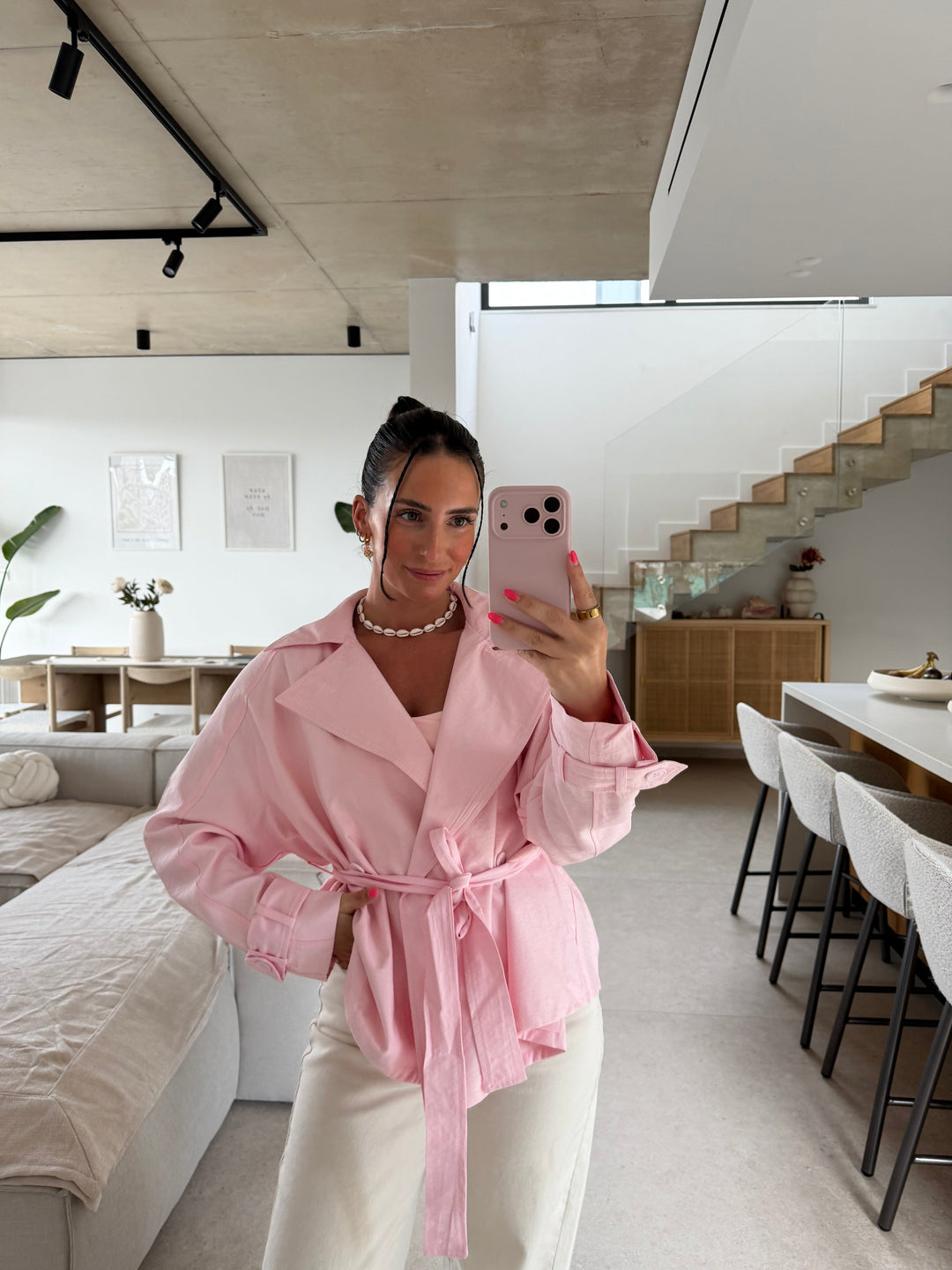 Frau im kurzen Trenchcoat in Rosa mit breitem Revers, vorne zur Schleife gebundenem Gürtel und Riegeln an den Ärmeln, dazu eine cremefarbene weite Hose | Lisa’s Boutique