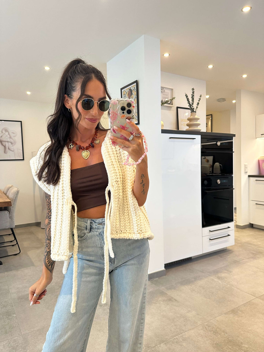 Modell trägt eine braune Weste aus Kunstleder über einer geblümten, langärmeligen Bluse mit Leopardenmuster – kombiniert mit hellblauer High-Waist-Jeans, aufgenommen im modernen Indoor-Ambiente.