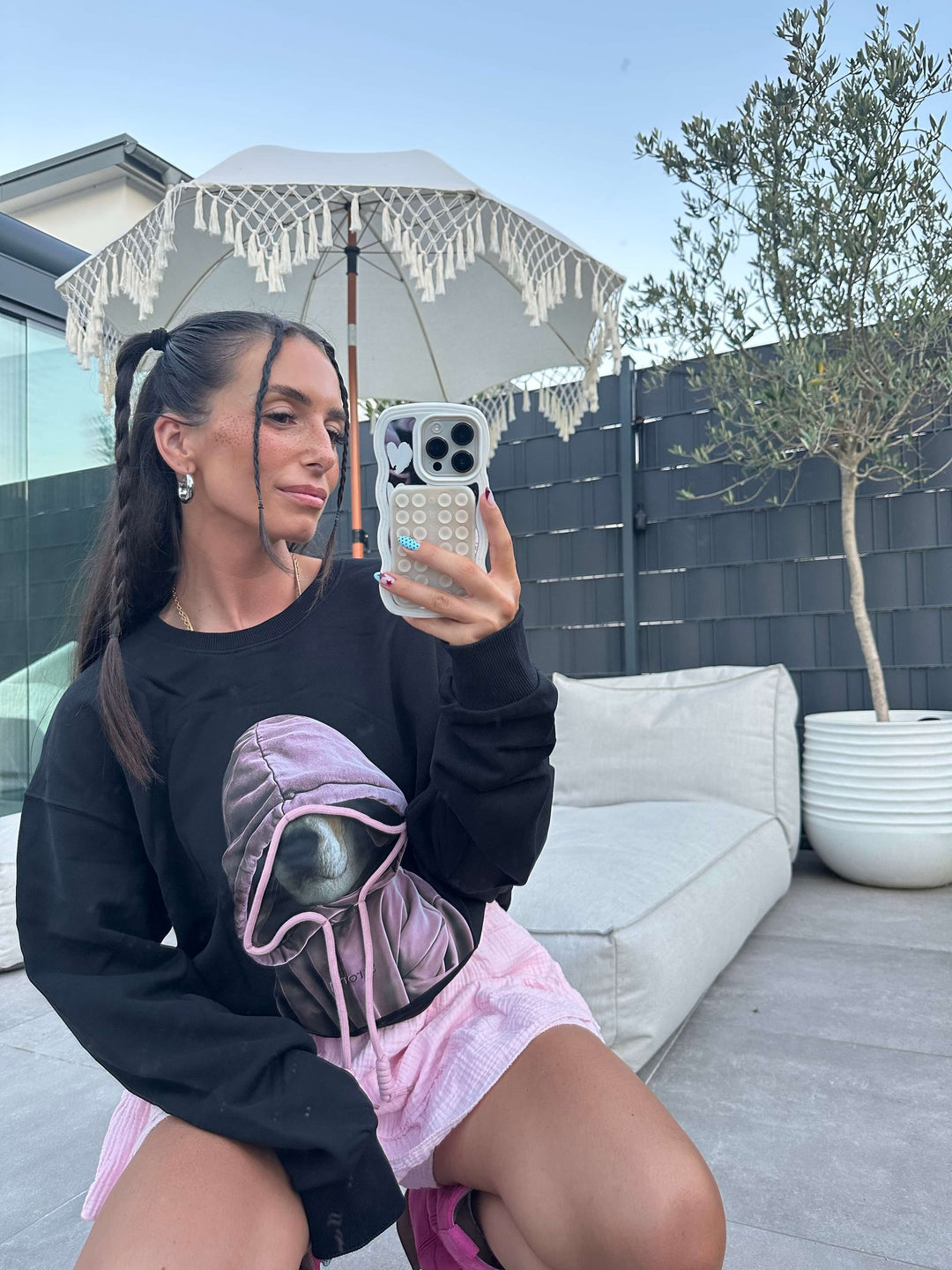 Frau trägt schwarzen Sweater mit großem grafischem Kapuzenprint auf der Vorderseite, kombiniert mit rosa Rock.
