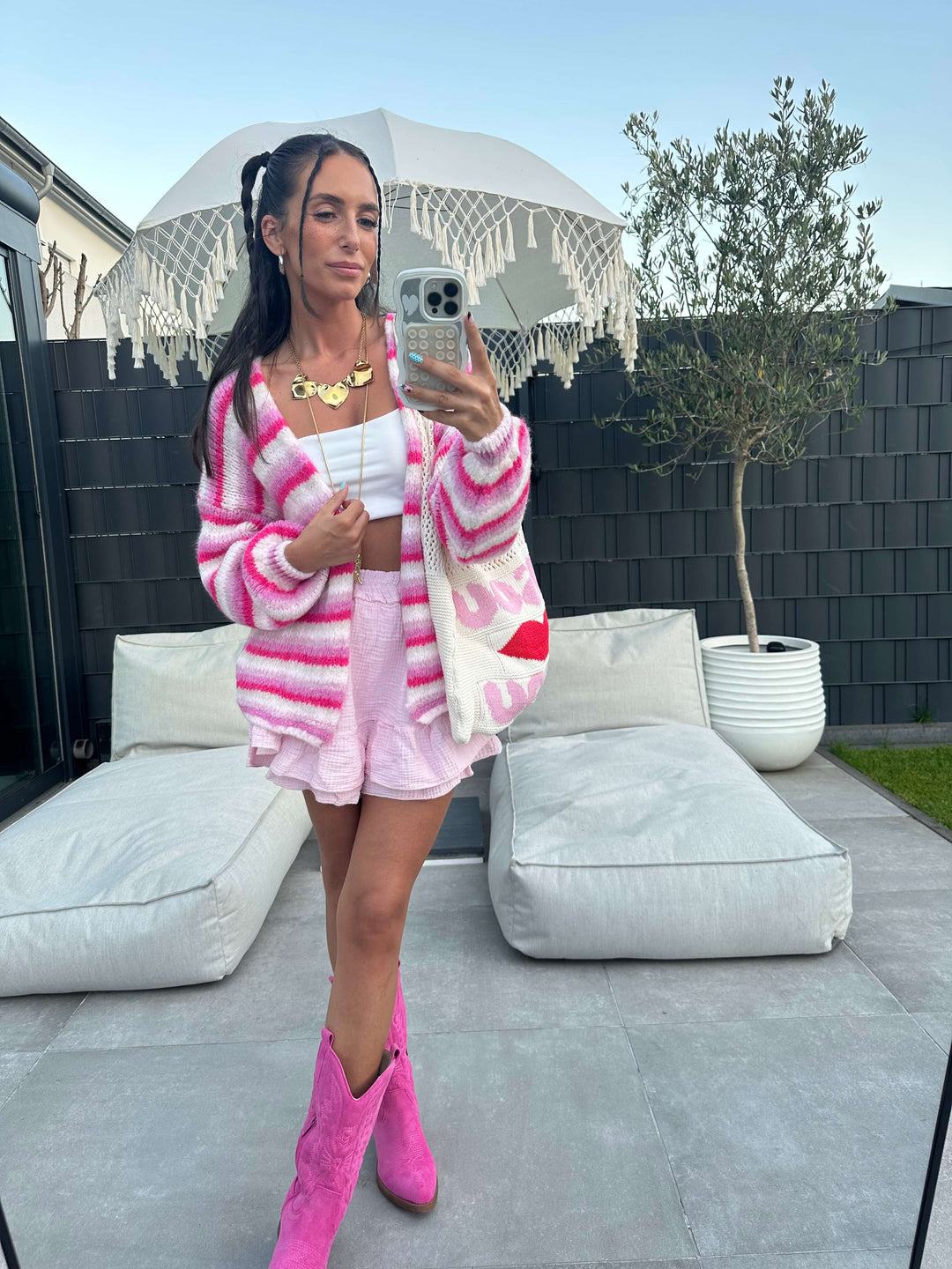 Komplettansicht eines pink-weiß gestreiften Strick-Sets mit passender Strickjacke, Minirock, weißem Crop-Top, pinken Cowboy-Stiefeln und großer Netz-Shopper-Tasche mit rotem Kussmund-Print.