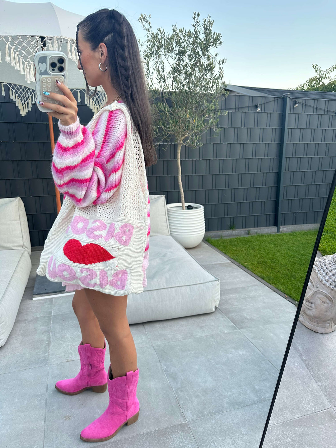 Seitenansicht eines pink-weiß gestreiften Strick-Sets mit passender Strickjacke, Minirock, pinken Cowboy-Stiefeln und großer Netz-Shopper-Tasche mit rotem Kussmund-Print.