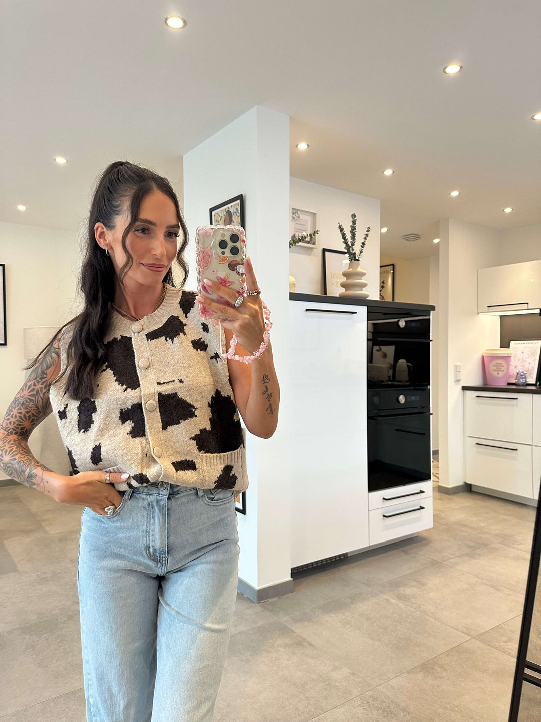 Model trägt eine ärmellose Strickweste mit Kuhmuster in Schwarz-Weiß und großen Knöpfen, kombiniert mit hellblauer High-Waist-Jeans.