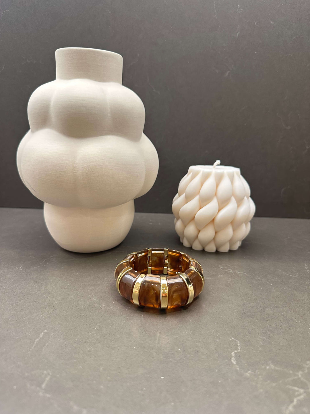 Breites braun-goldenes Armband im Luxuslook vor skulpturalen Deko-Kerzen