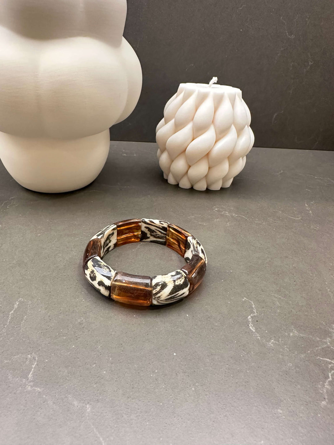 Stretch-Armband mit braunen Gliedern und Zebra-Muster vor weißen Dekokerzen