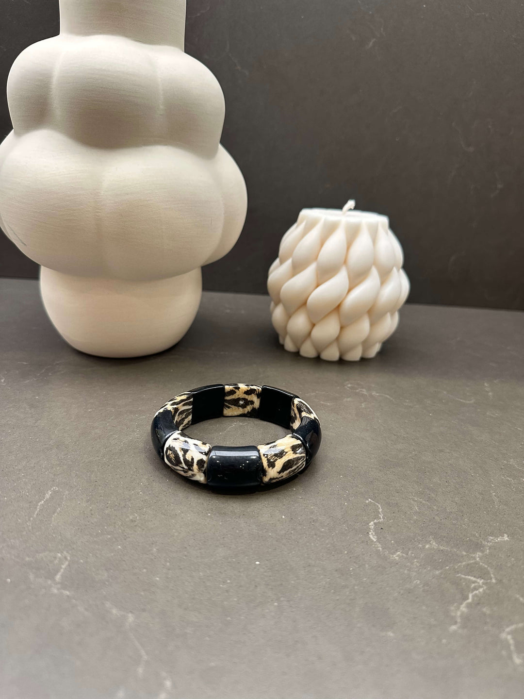 Schwarz-glänzendes Stretch-Armband mit Leo-Print vor weißen Deko-Kerzen