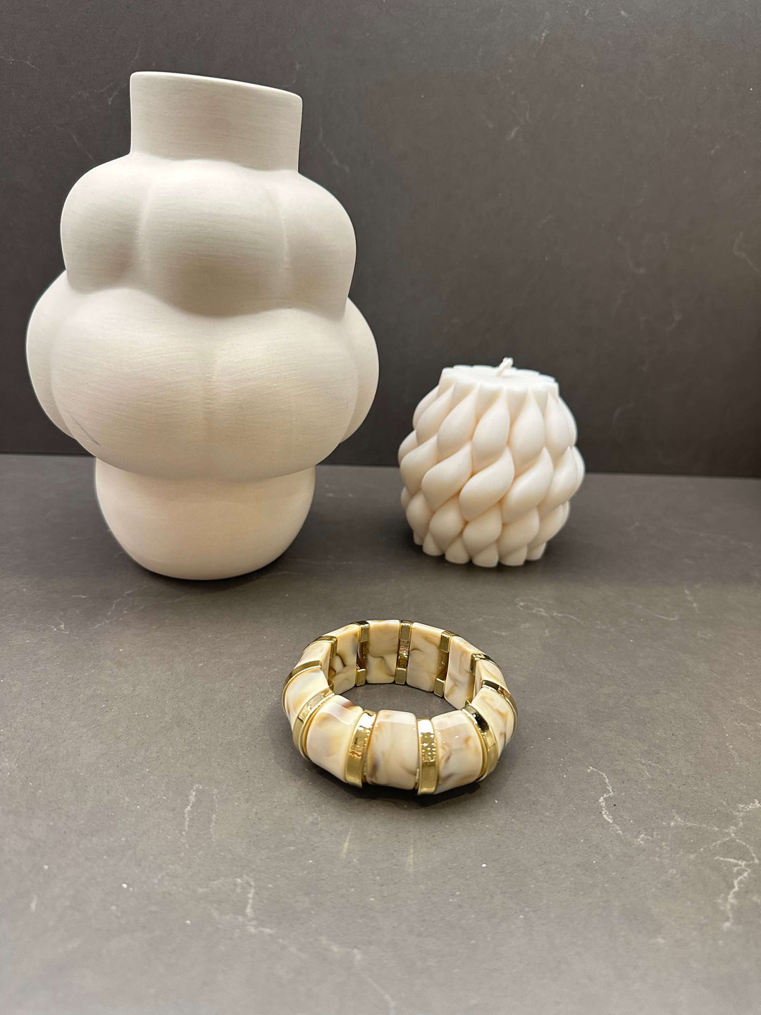 Stretch-Armband in Marmorweiß mit goldenen Gliedern vor dekorativen Kerzen