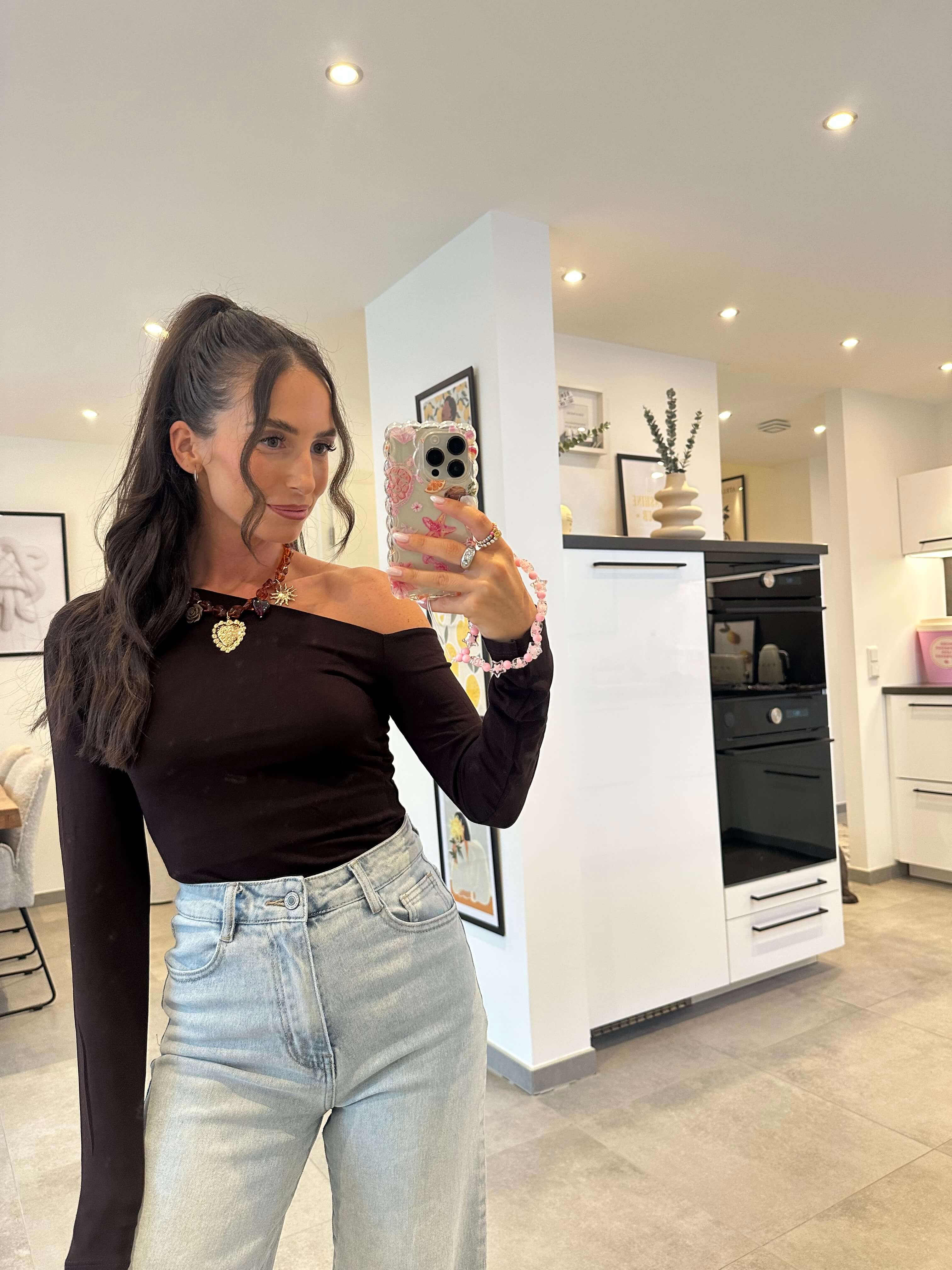 Frau trägt schwarzes asymmetrisches One-Shoulder-Top mit langem Ärmel und High-Waist-Jeans