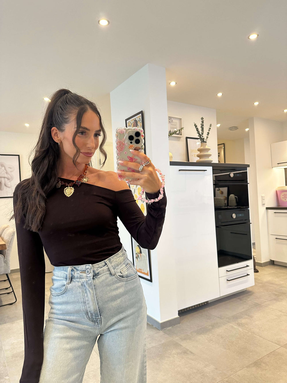 Frau trägt schwarzes asymmetrisches One-Shoulder-Top mit langem Ärmel und High-Waist-Jeans