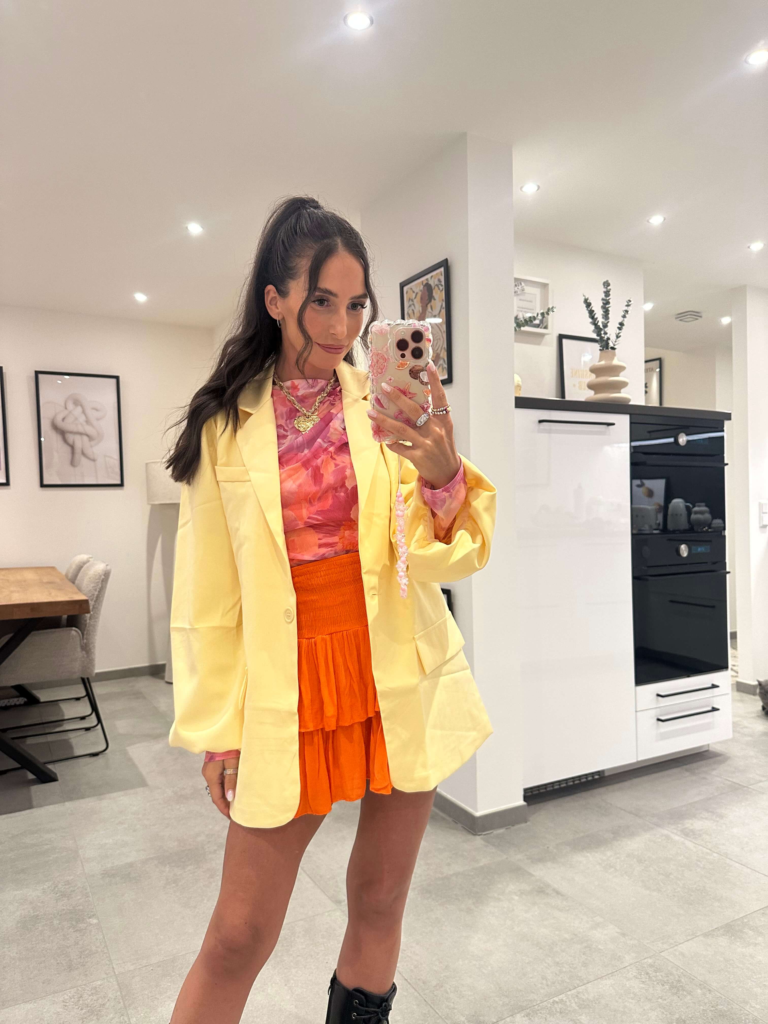 Frau trägt zitronengelben Blazer mit Knopf über orangem Sommeroutfit