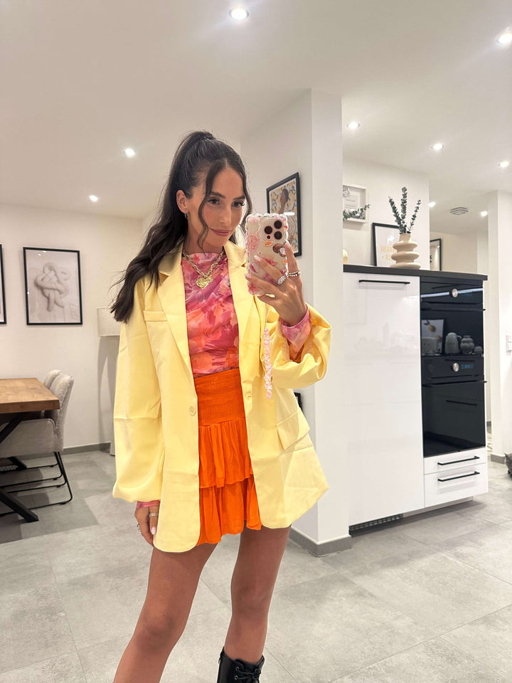 Frau trägt zitronengelben Blazer mit Knopf über orangem Sommeroutfit