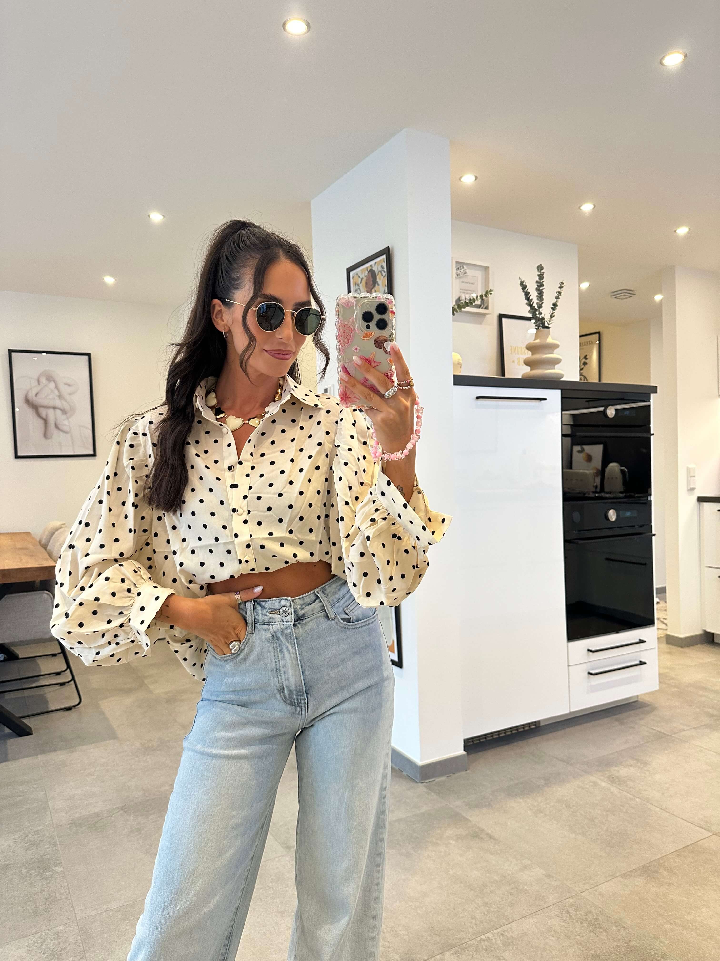 Crop Bluse in Weiß mit buntem Polka-Dot-Muster, weiten Ärmeln und Gummibund, getragen zur hellblauen Jeans.