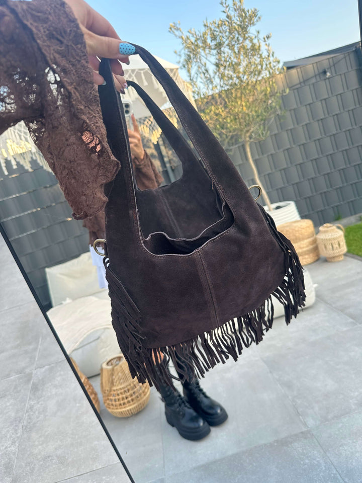 Detailaufnahme einer braunen Fransentasche in Wildleder-Optik, in der Hand gehalten, mit sichtbarer Fransenverzierung am Taschenboden.