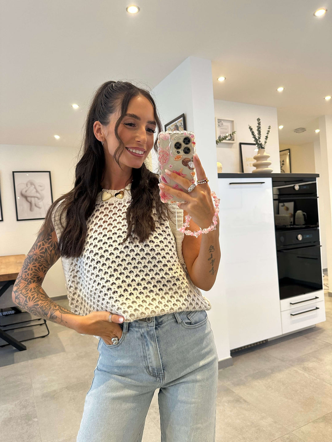 Frau trägt ein ärmelloses, weißes Häkel-Top mit lockerer Passform und Vintage-Vibes, kombiniert mit einer High-Waist-Jeans