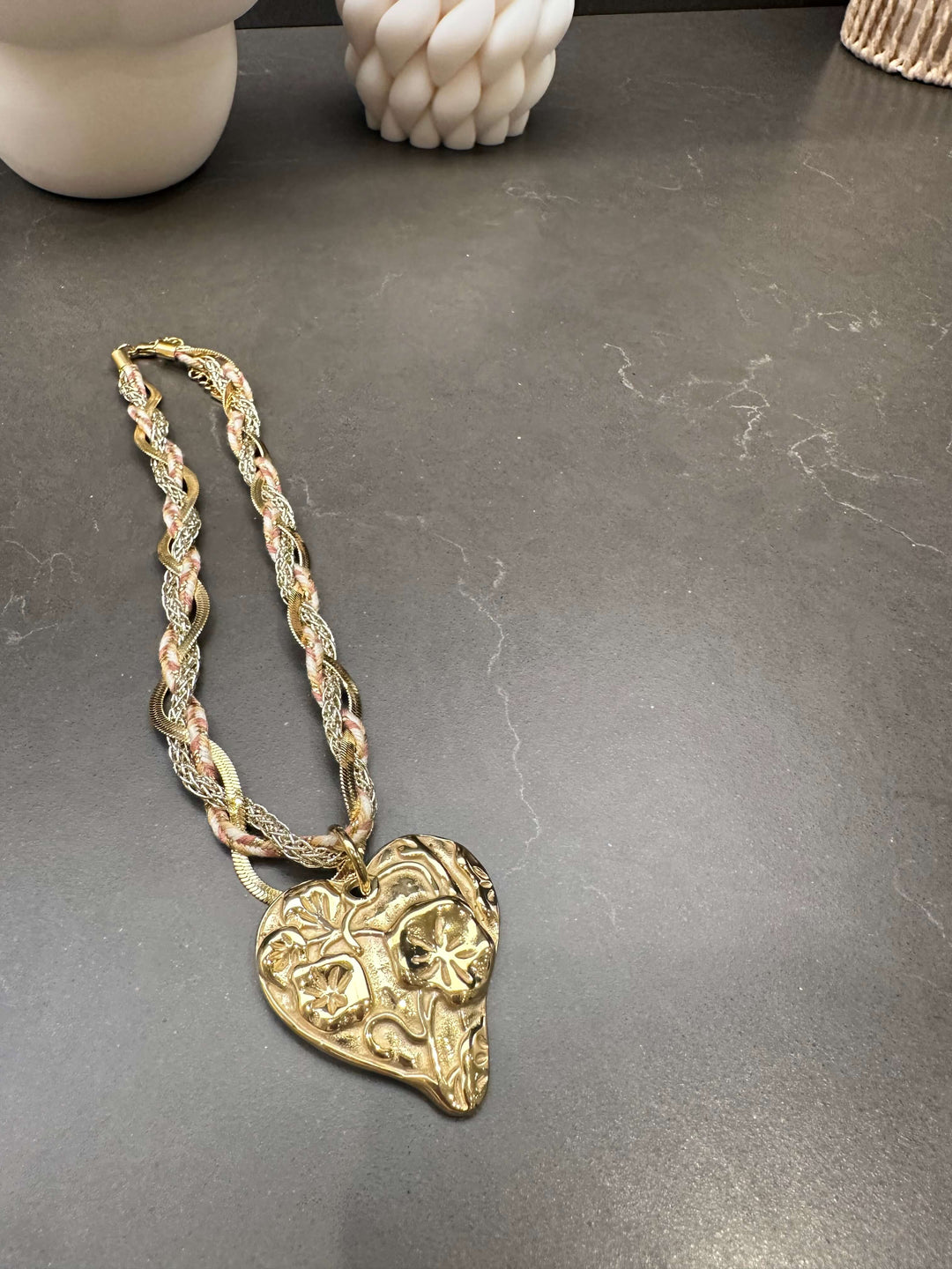 Goldene Kette mit herzförmigem Ornament-Anhänger auf dunkler Marmoroberfläche vor Dekokerzen