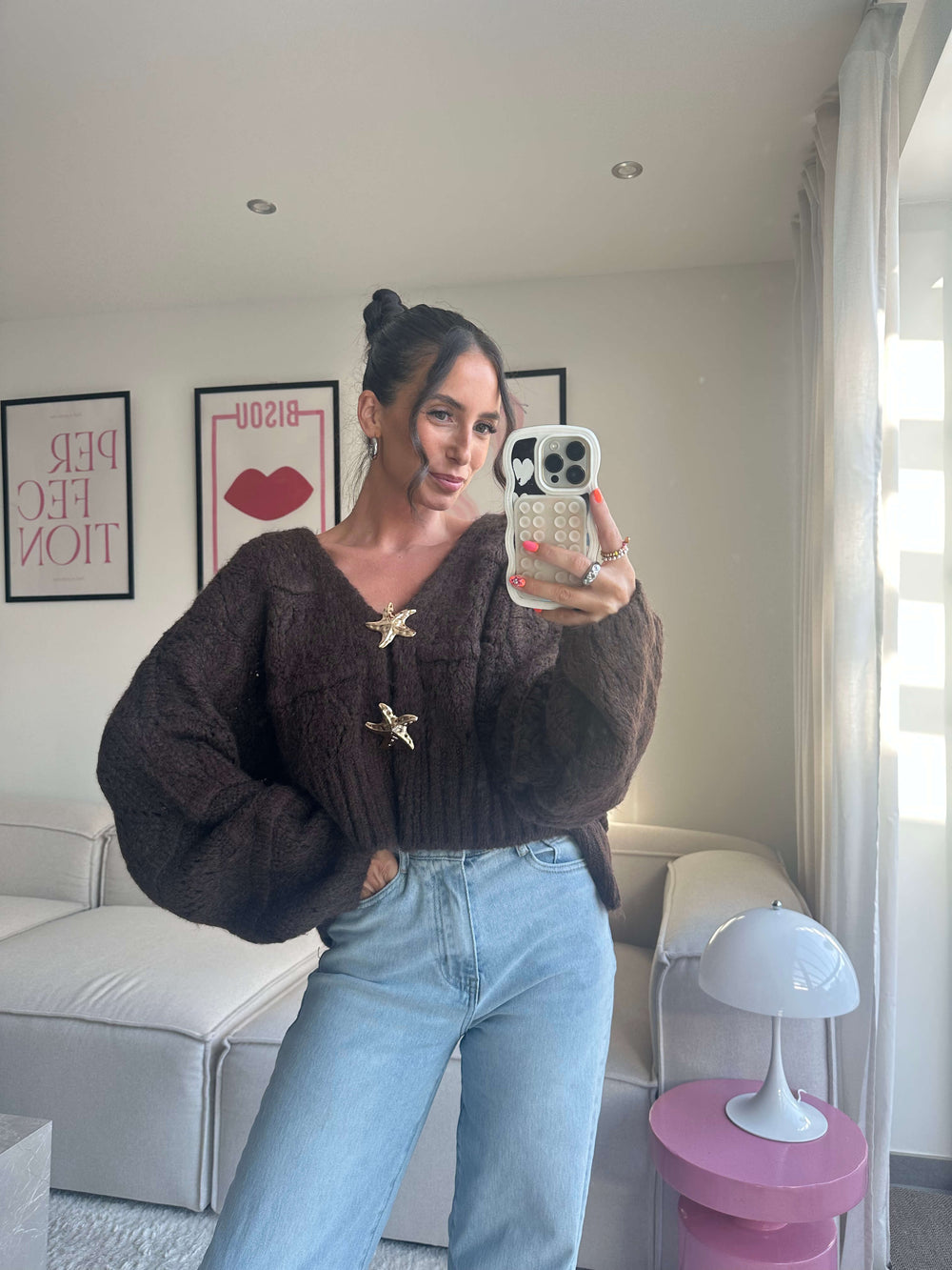 Lisa trägt einen braunen Strickcardigan mit voluminösen Ärmeln und goldenen Broschen, kombiniert mit einer hellblauen Jeans – Lisas Boutique
