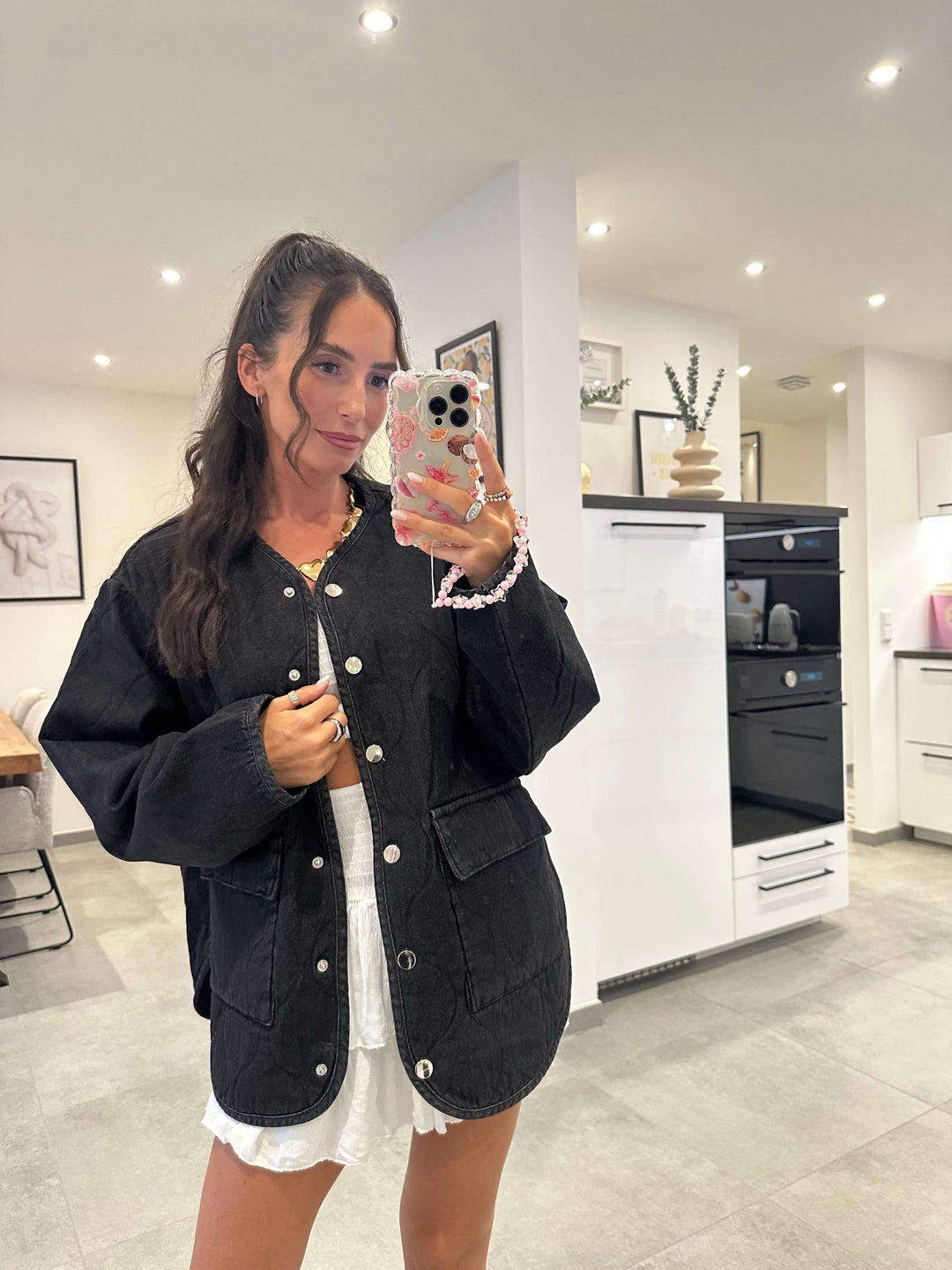 Frau trägt oversized schwarze Jacke mit Knopfleiste über weißem Kleid