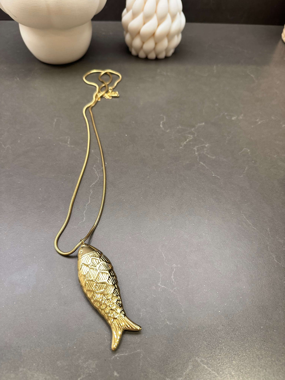Goldene Kette mit detailreichem Fisch-Anhänger auf dunklem Untergrund
