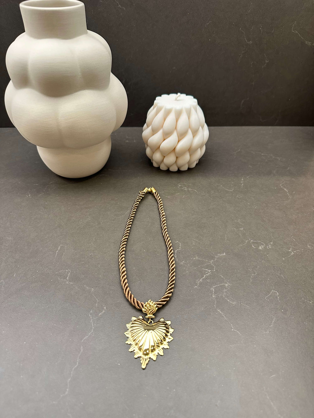 Goldene Kette mit großem Muschelherz-Anhänger und gedrehtem Band auf dunkler Oberfläche