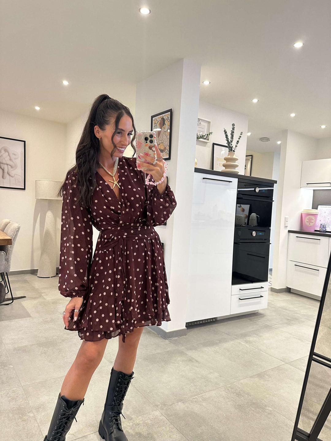 Model trägt ein bordeauxfarbenes Kleid mit weißen Punkten, V-Ausschnitt und Volant-Saum – kombiniert mit schwarzen Boots für einen femininen und gleichzeitig lässigen Alltagslook.