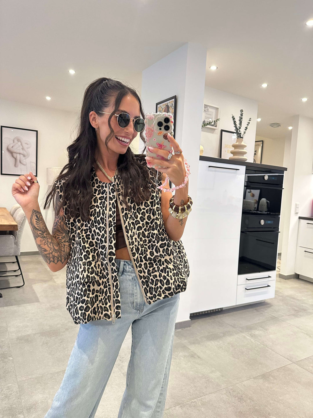 Frau trägt eine flauschige Leopardenweste in Beige-Braun mit lockerer Passform über einem Top und einer hellblauen Jeans.