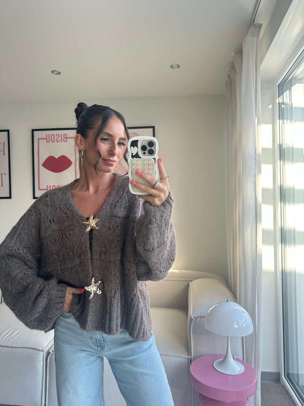 Lisa präsentiert einen tauben Strickcardigan mit weiten Ärmeln und goldfarbenen Broschen, kombiniert mit einer hellblauen Jeans – Lisas Boutique