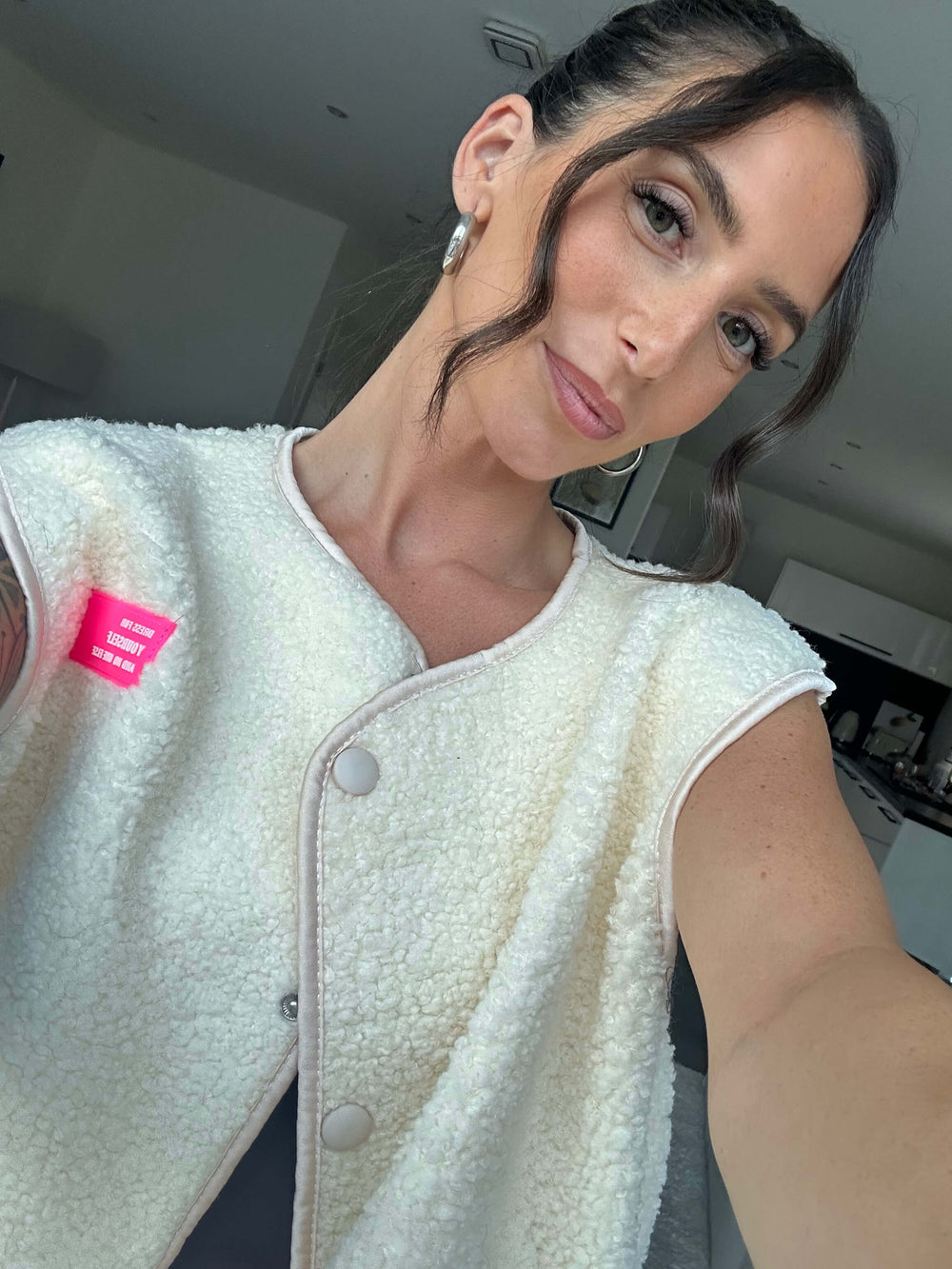 Lisa trägt eine ärmellose cremefarbene Flauschweste mit Rundhalsausschnitt und Knopfverschluss, kombiniert mit schwarzem Oberteil – Lisas Boutique