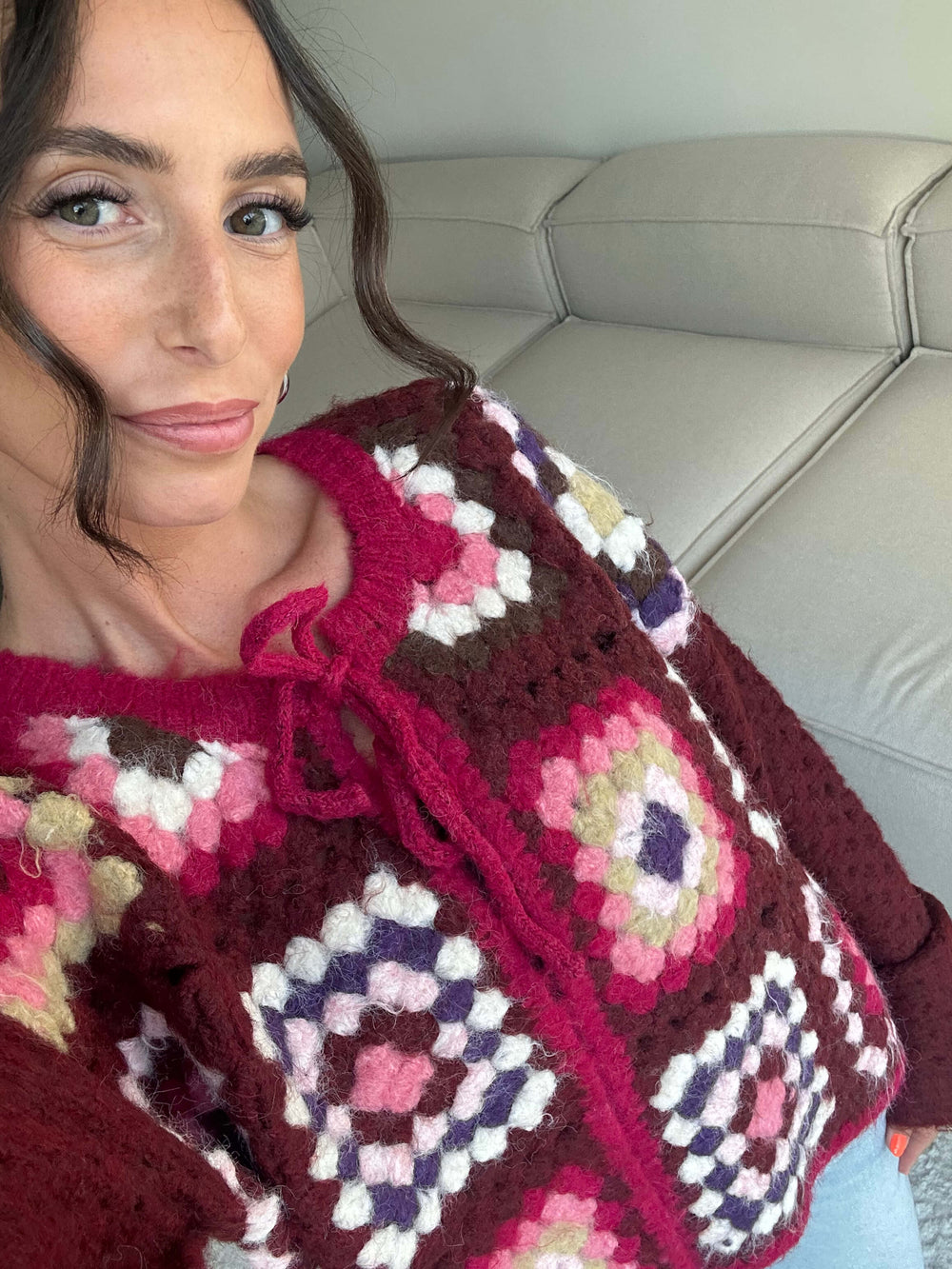 Lisa trägt einen bordeauxfarbenen, gehäkelten Cardigan mit farbigem Patchwork-Muster und Schleifenverschluss – Lisas Boutique