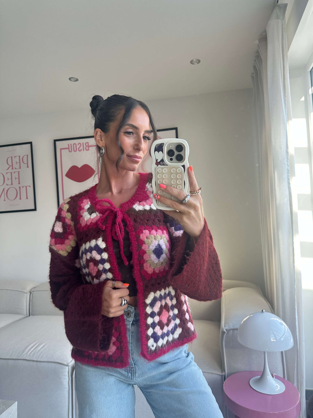 Lisa trägt einen bordeauxfarbenen, gehäkelten Cardigan mit buntem Patchworkmuster und Schleifenverschluss vorne – Lisas Boutique