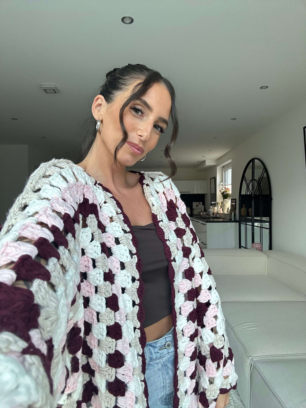 Lisa trägt einen langen, gehäkelten Cardigan in Creme und Braun mit großem Blumenmuster, kombiniert mit schwarzem Top und hellblauer Jeans – Lisas Boutique