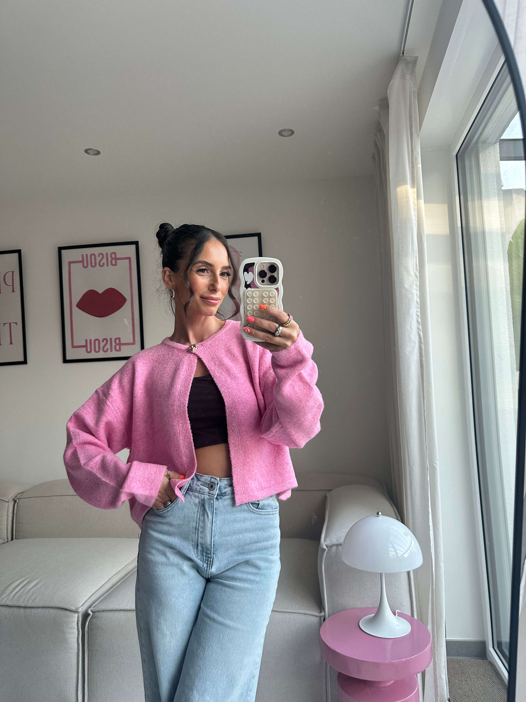 Lisa trägt einen kurzen, pinkfarbenen Strickbolero mit Hakenverschluss, kombiniert mit schwarzem Crop-Top und hellblauer Jeans – Lisas Boutique