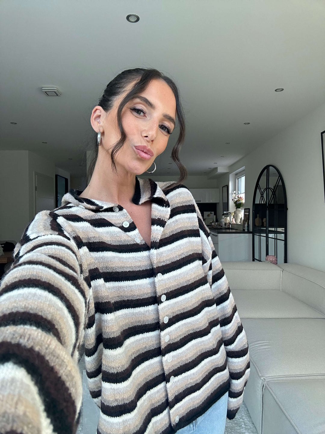 Lisa trägt einen gestreiften Strickcardigan in Beige, Schwarz und Creme mit Knopfleiste, kombiniert mit hellblauer Jeans – Lisas Boutique