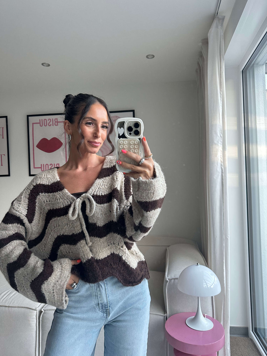 Lisa trägt einen kuscheligen Strickcardigan in Braun-Creme-Streifen mit Schleifenverschluss vorne, kombiniert mit hellblauer Jeans – Lisas Boutique