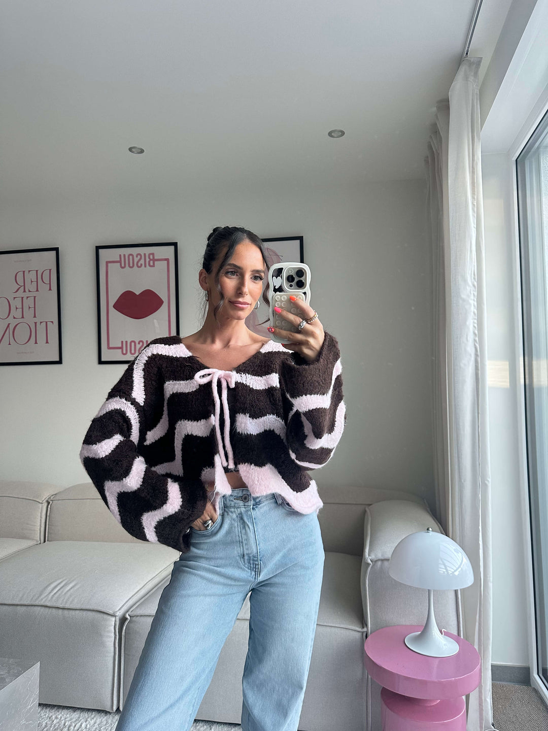 Lisa trägt einen Strickcardigan in Braun-Creme mit wellenförmigem Muster und Schleifenverschluss, kombiniert mit hellblauer Jeans – Lisas Boutique