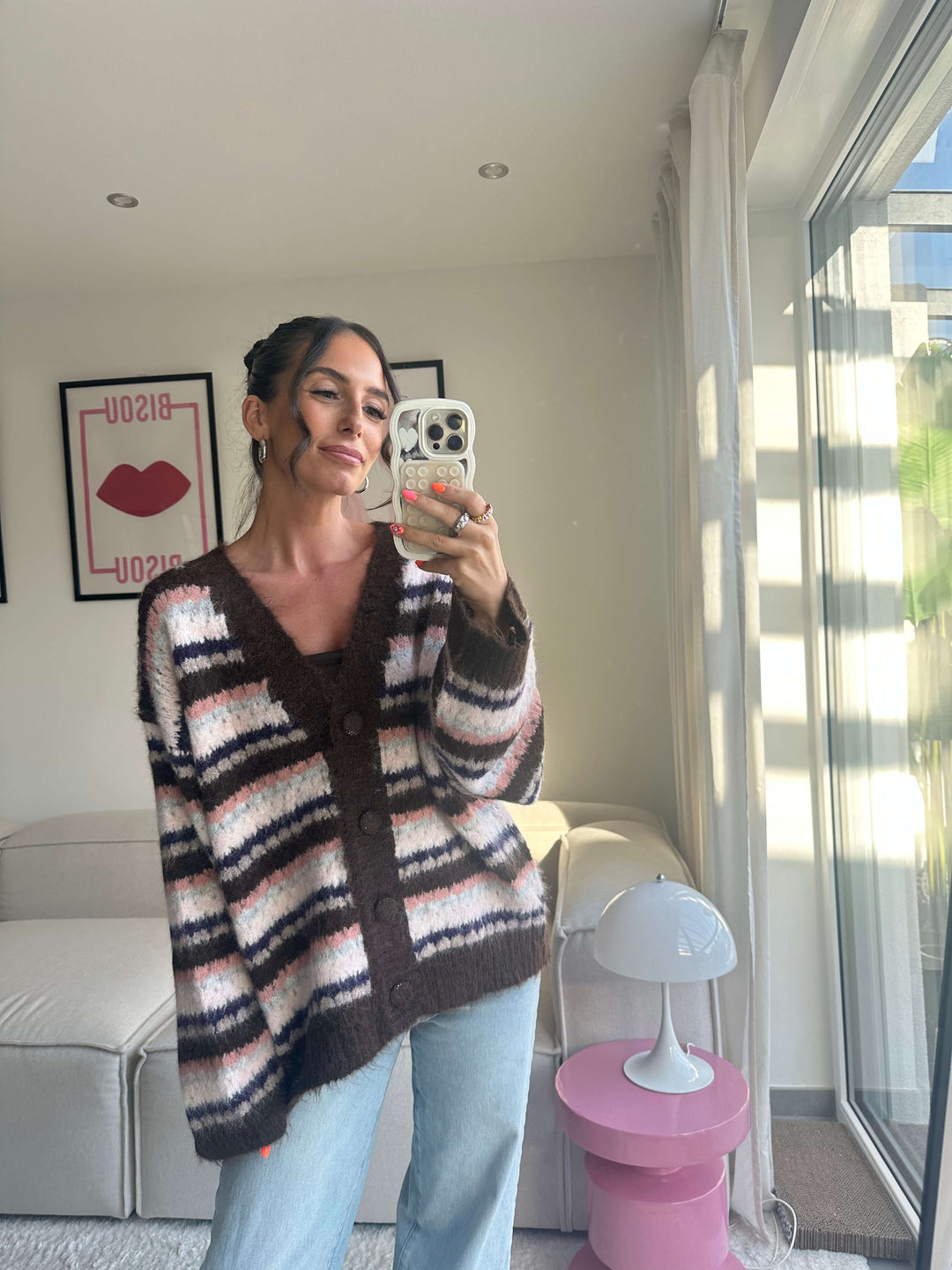 Lisa trägt einen langen, kuscheligen Strickcardigan in Braun, Rosa und Schwarz gestreift mit Knopfleiste, kombiniert mit hellblauer Jeans – Lisas Boutique