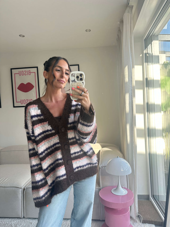 Lisa trägt einen langen, kuscheligen Strickcardigan in Braun, Rosa und Schwarz gestreift mit Knopfleiste, kombiniert mit hellblauer Jeans – Lisas Boutique