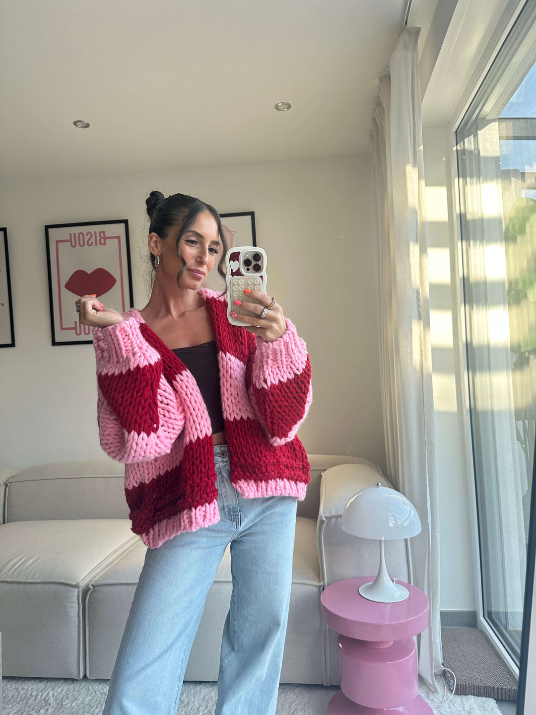 Lisa trägt einen grob gestrickten Cardigan in Rot und Pink mit breiten Streifen, kombiniert mit schwarzem Top und hellblauer Jeans – Lisas Boutique