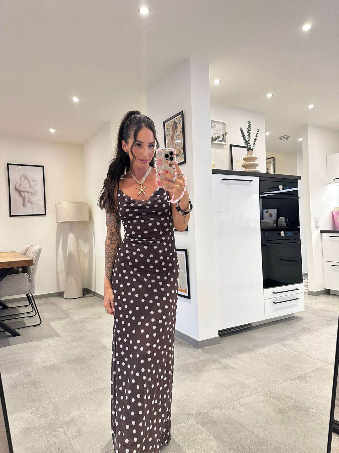 Model trägt ein langes, schwarzes Maxikleid mit weißen Punkten und Spaghettiträgern