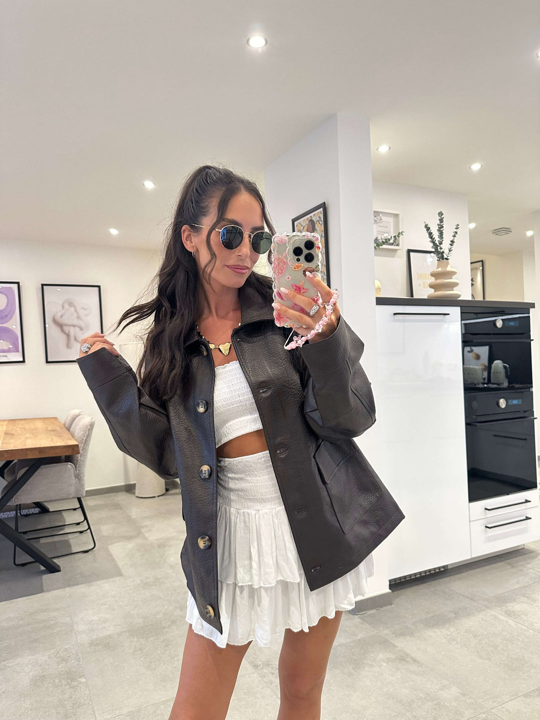 Model trägt eine oversized schwarze Lederjacke mit goldenen Knöpfen – kombiniert mit einem weißen Sommer-Set für einen stilvollen Kontrast-Look.