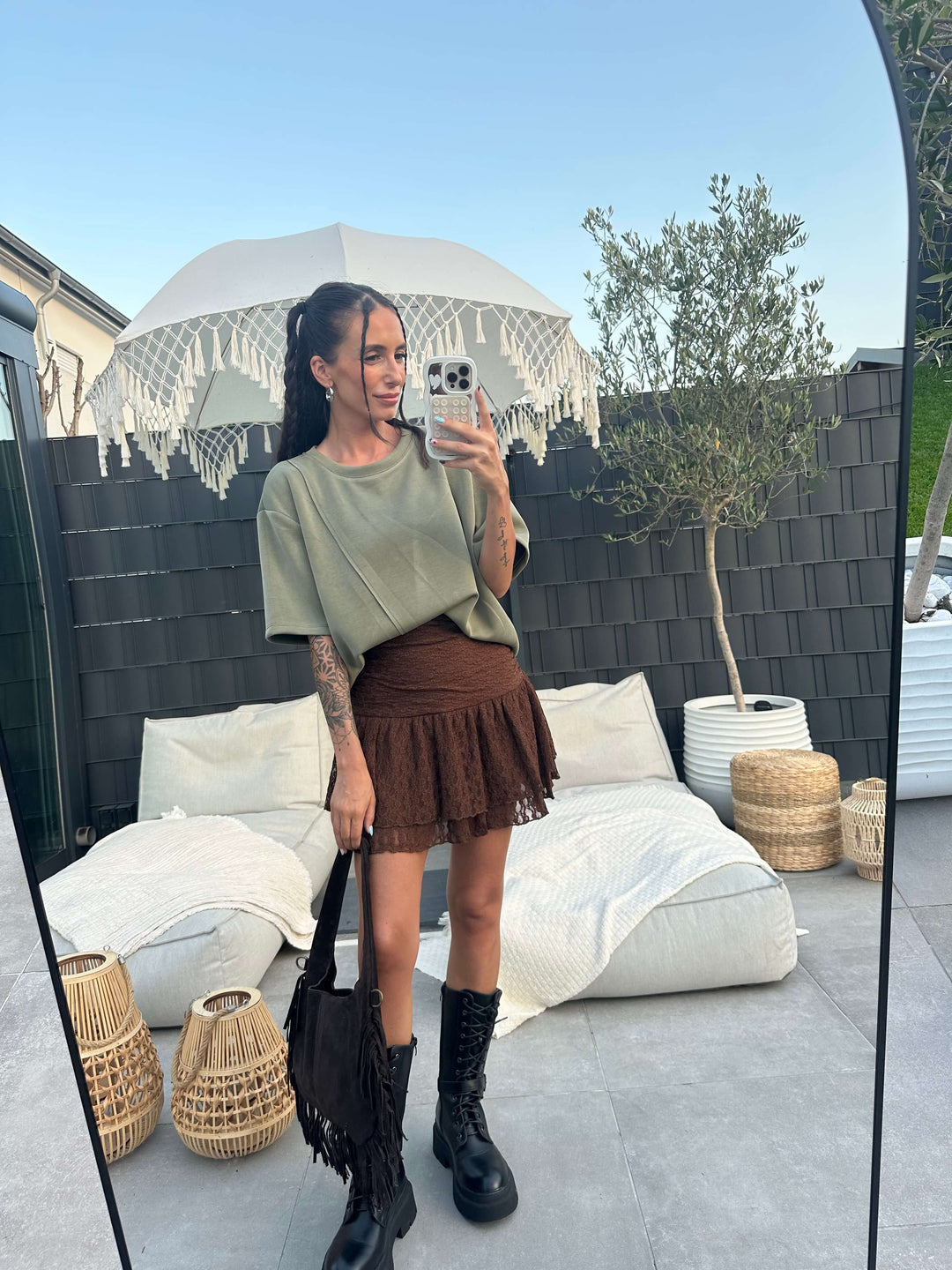 Locker geschnittenes Oversize-T-Shirt in Grün, kombiniert mit braunem Minirock und Fransentasche im Outdoor-Bereich.