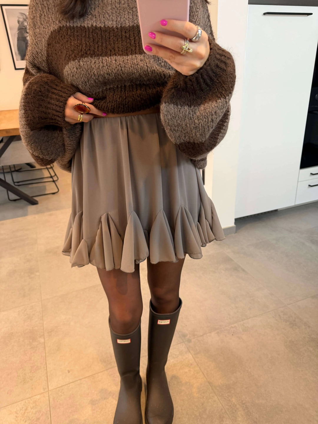 Falda corta color topo para mujer con volante en el bajo, foto al espejo con jersey de rayas marrones y botas altas