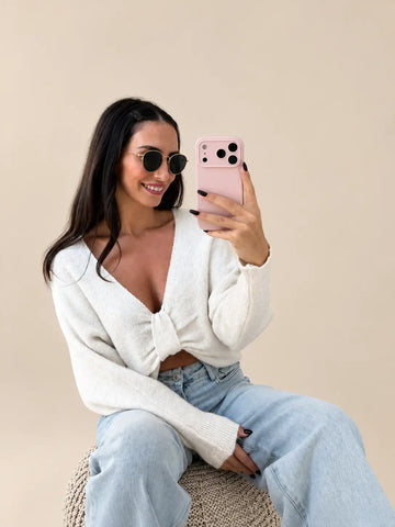 Pull à nœud femme beige à décolleté en V profond, assise avec un jean clair | Lisa’s Boutique